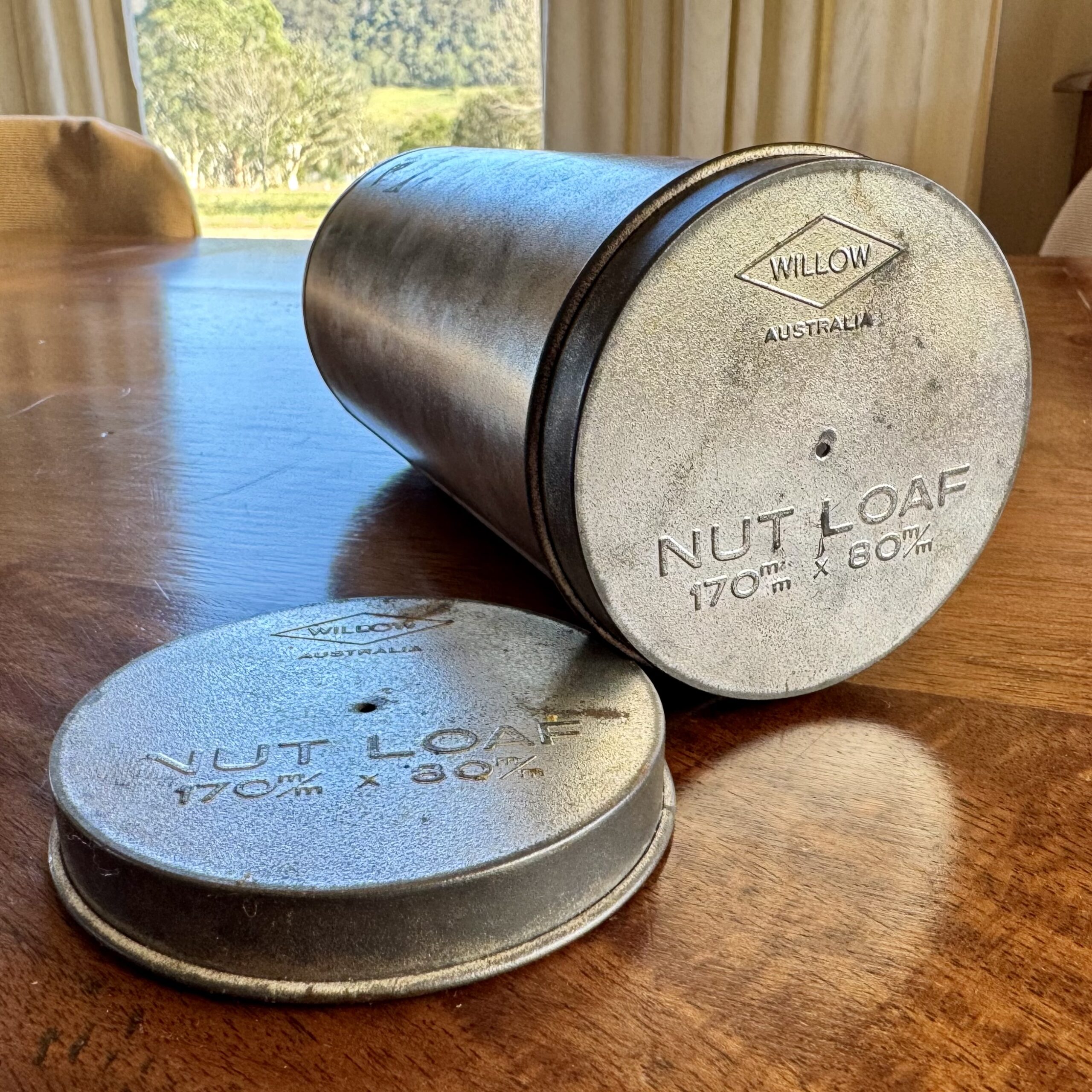 Cylindrical metal tin and detached lid made by Willow sitting on a wooden table 
